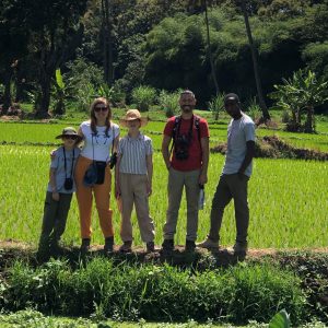 Four people are gathered in front of a sprawling rice field, emphasizing the connection between community and nature.