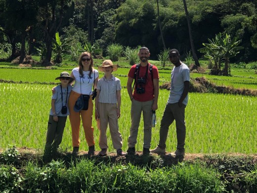 Four people are gathered in front of a sprawling rice field, emphasizing the connection between community and nature.