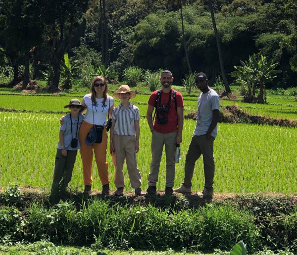 Four people are gathered in front of a sprawling rice field, emphasizing the connection between community and nature.