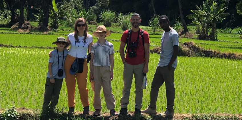 Four people are gathered in front of a sprawling rice field, emphasizing the connection between community and nature.