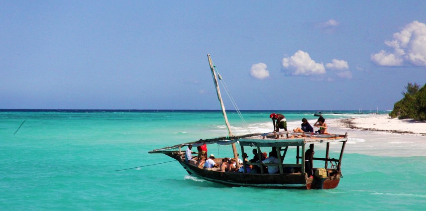 4 Days Zanzibar Paradise marine adventure. A sailboat glides across the turquoise waters of the Indian Ocean, with the white sandy beaches of Zanzibar in the distance.