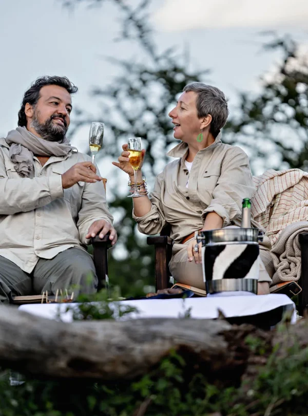 A romantic couple enjoying champagne by a cozy fireplace in the Serengeti, surrounded by the beauty of nature.