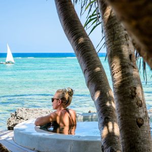 A woman enjoying a serene beach view in Zanzibar, standing near a beach bed with soft white linens