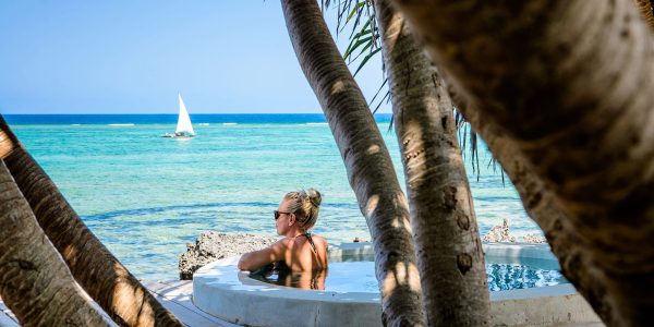 A woman enjoying a serene beach view in Zanzibar, standing near a beach bed with soft white linens