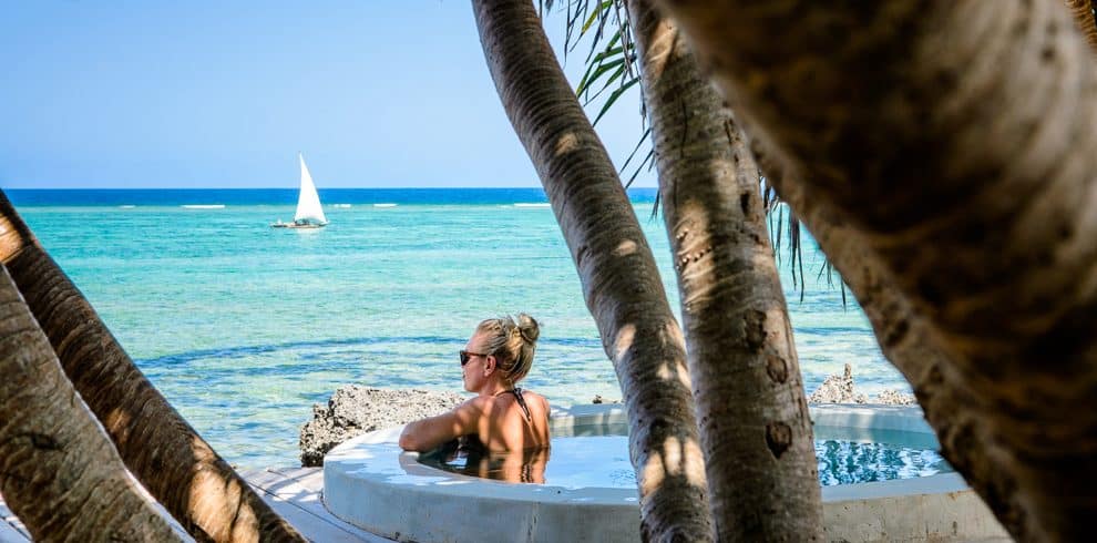 A woman enjoying a serene beach view in Zanzibar, standing near a beach bed with soft white linens